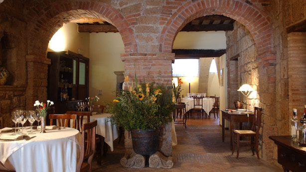 Ein Restaurant mit Backsteinbögen, Tischen mit weißen Tischdecken und einer zentralen Blumenkomposition.
