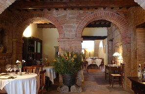 A restaurant with brick arches, tables set with white tablecloths, and a central flower arrangement. - Albergo Scilla (Sorano)