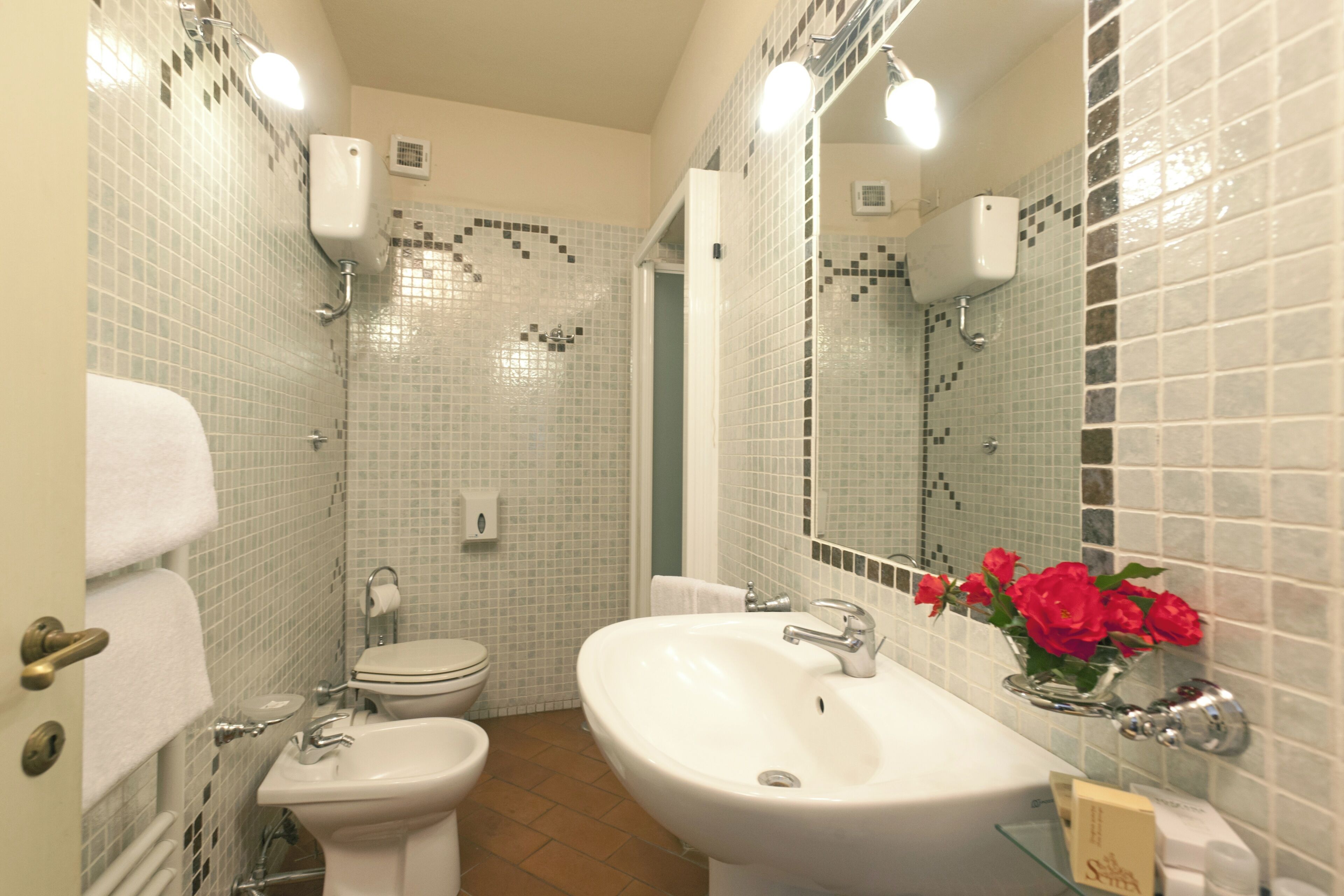 Ein Badezimmer mit Toilette, Bidet, Waschbecken und einem Spiegel mit Blumen.
