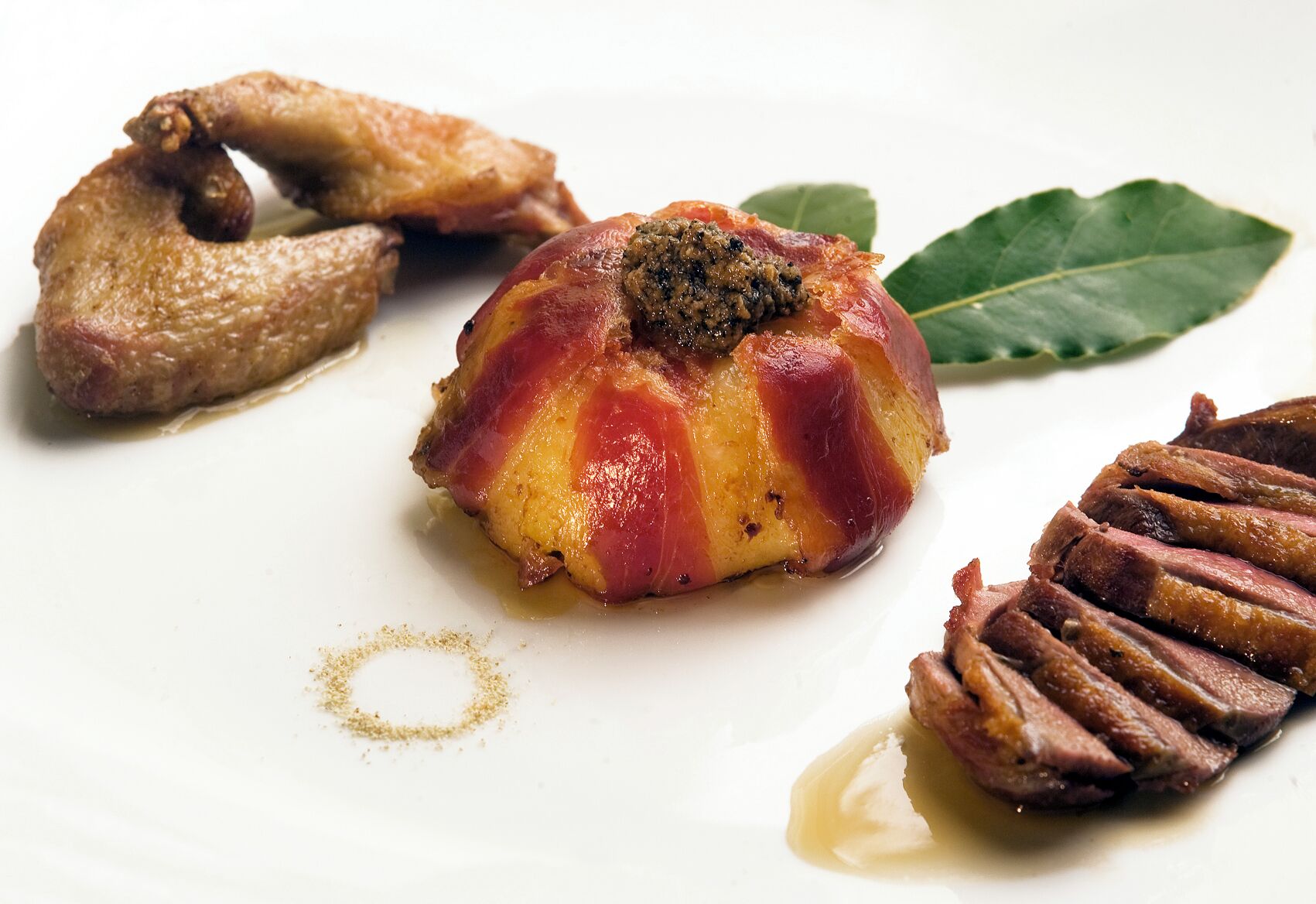 Un piatto con forma sferica, una porzione di carne con condimento scuro e una fetta di carne su un piatto bianco.