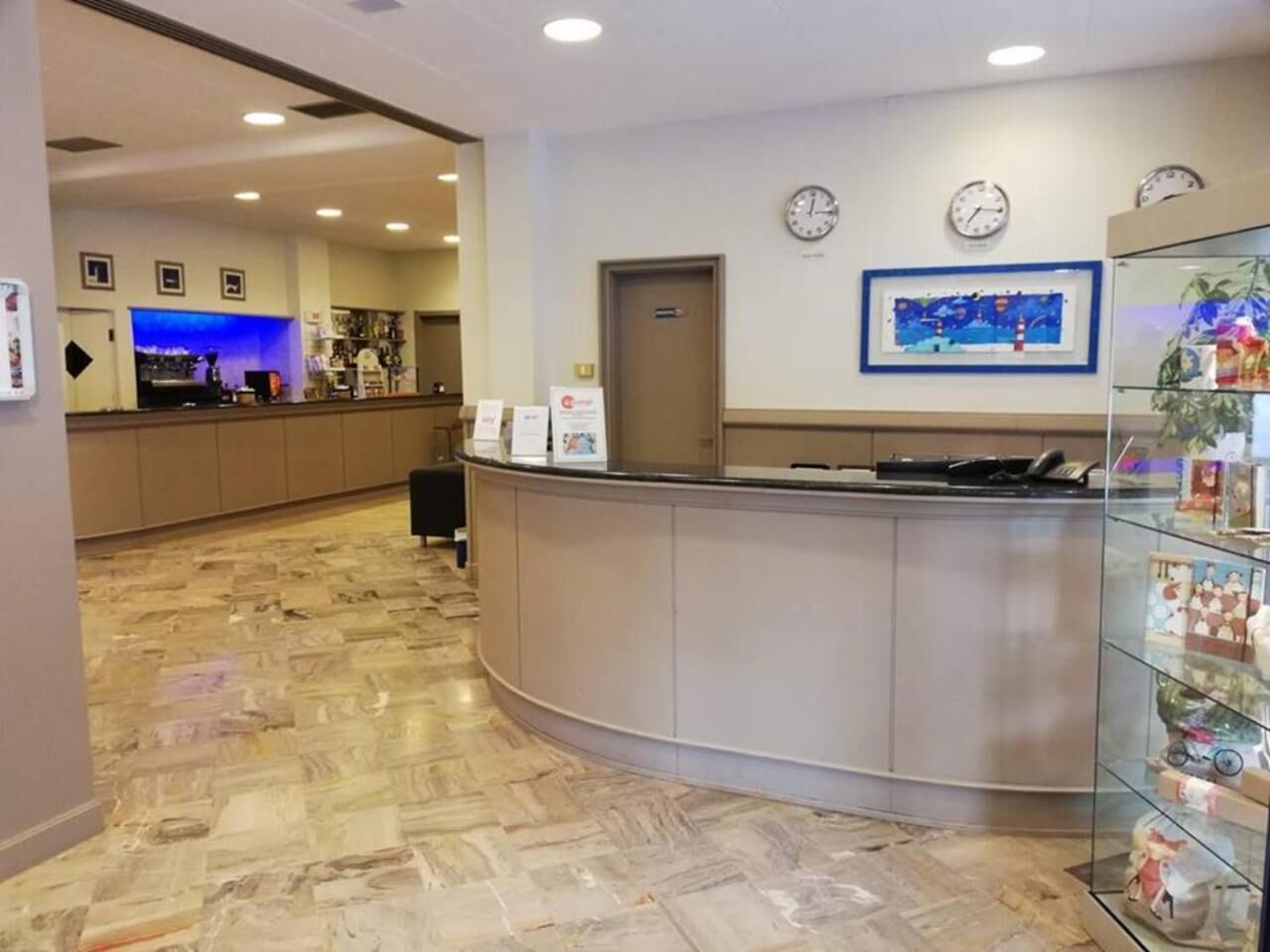 A hotel reception area with a curved reception desk, a glass display case with items, and a clock on the wall.