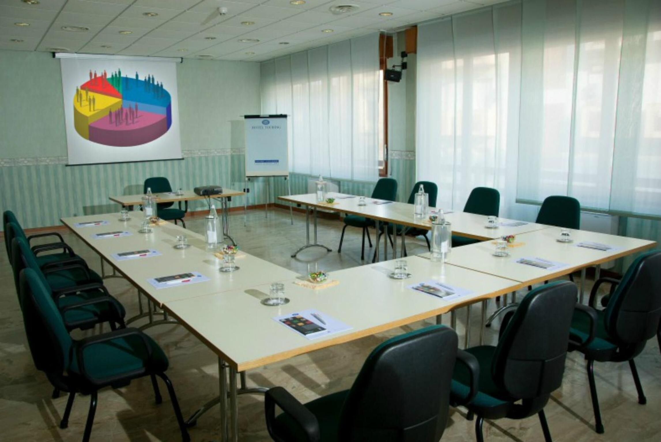 A conference room with a long table, chairs, a projector screen, and a whiteboard.