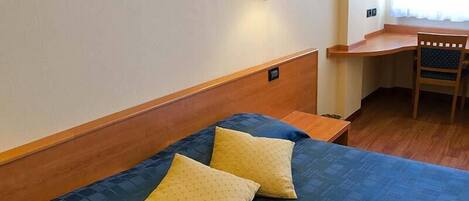 A hotel room with a bed, two pillows, a nightstand, a desk, and a chair.