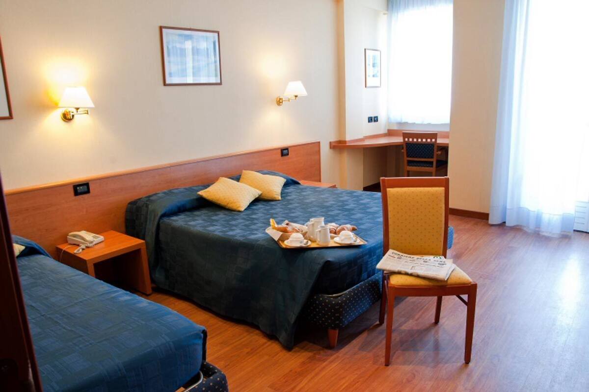 Ein Hotelzimmer mit Bett, Stuhl, Schreibtisch und einem kleinen Tisch mit Frühstücksgegenständen.