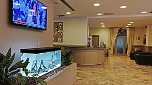 A hotel lobby with a reception desk, a television mounted on the wall, and a large aquarium with aquatic plants. - Hotel Touring Falconara Marittima (Falconara Marittima)