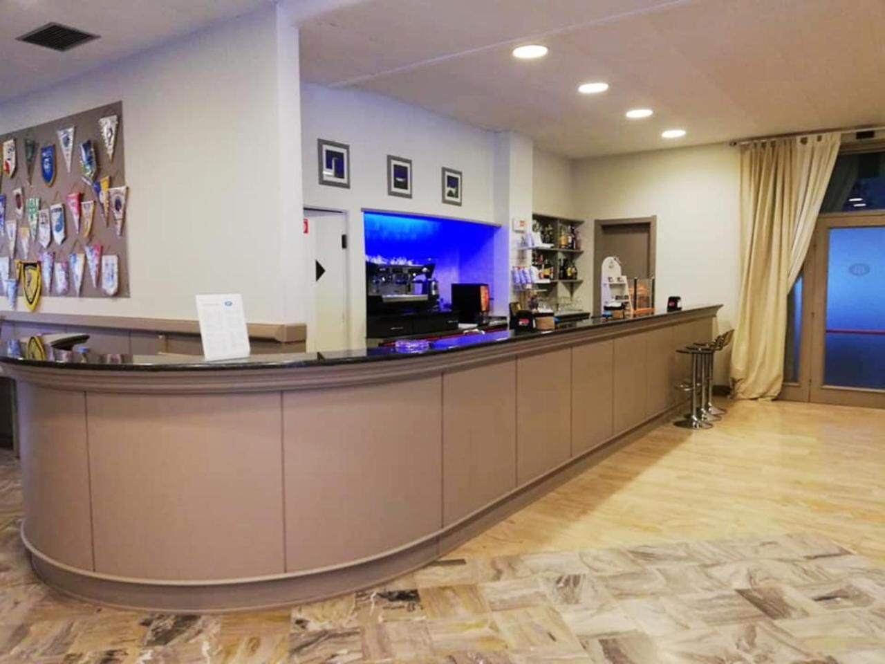 A reception area with a curved counter, a blue-lit bar, and a wall displaying various certificates.