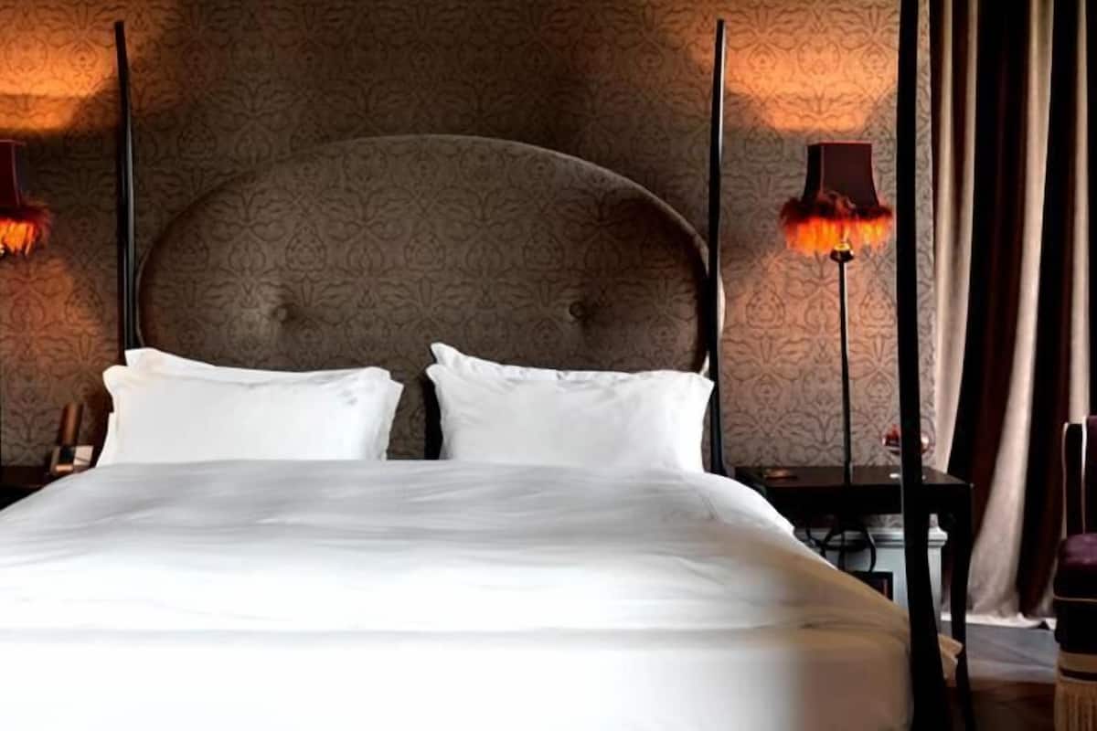 Ein Hotelzimmer mit einem großen Bett, zwei Nachttischen, einem Sessel und Tapete mit Muster.