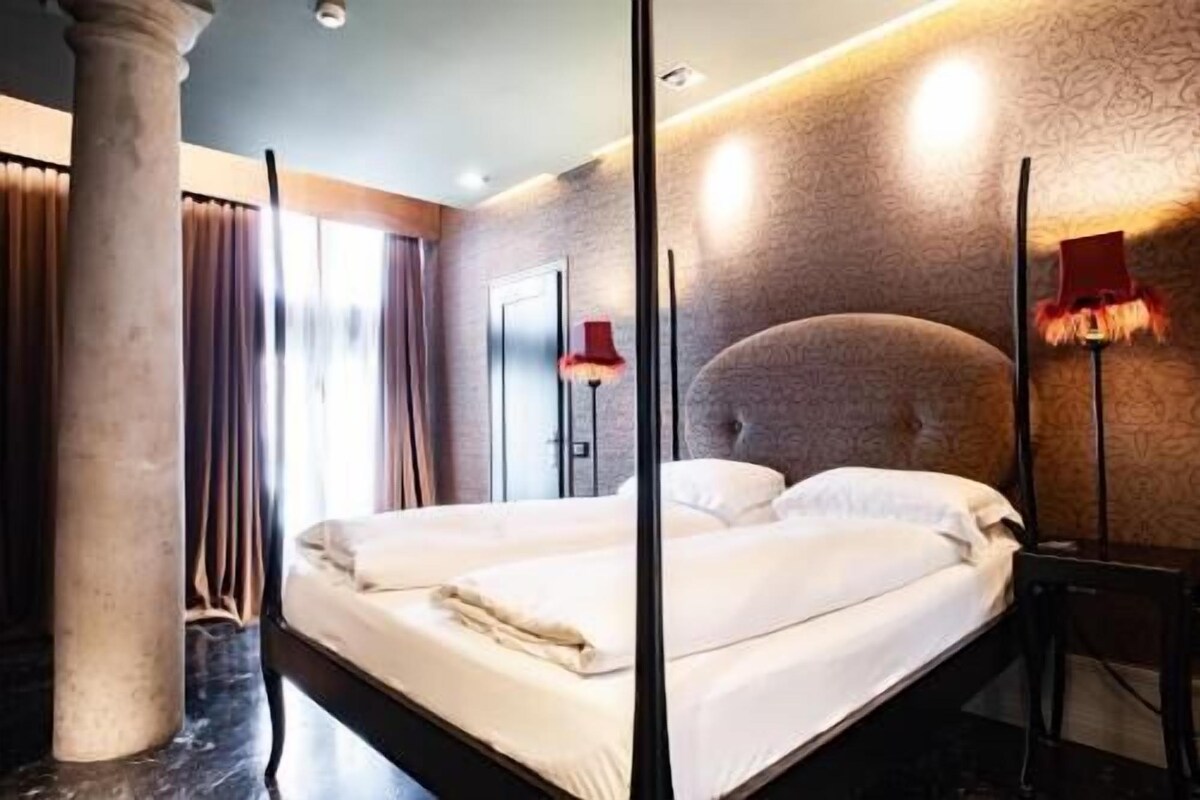 A modern hotel room with a large bed, a nightstand, a lamp, and a patterned wall.
