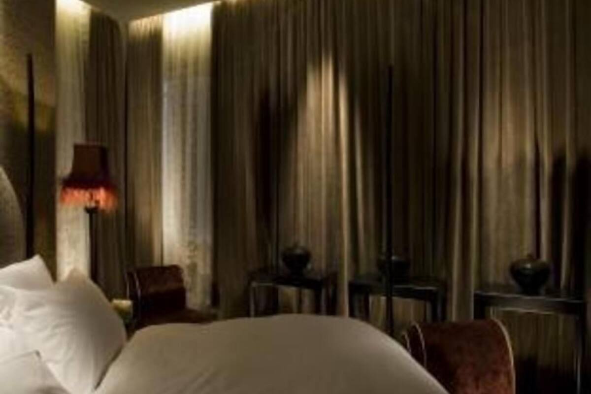 Ein Hotelzimmer mit Bett, Vorhängen, einer Lampe und einem Sessel.
