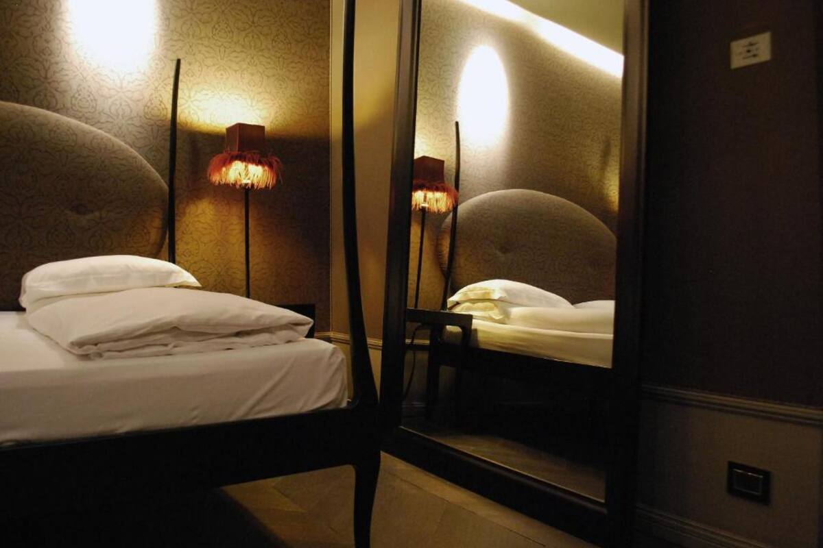 Ein Hotelzimmer mit einem Einzelbett, einem Nachttisch, einem Spiegel und zwei Wandleuchten.
