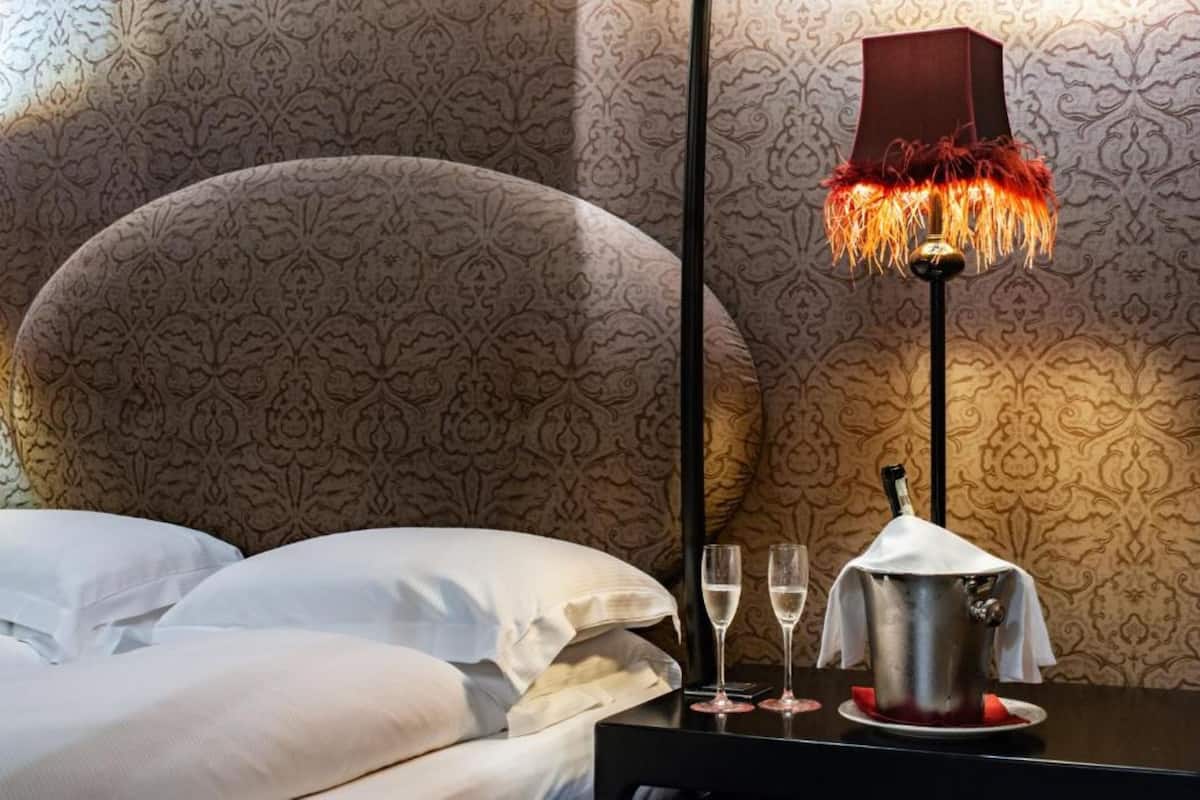 Ein ordentlich bezogenes Bett mit weißen Laken, ein schwarzer Nachttisch mit einer Lampe und zwei Gläser Wasser.