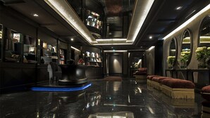 A modern lobby with a polished black floor, a reception desk, a seating area with red upholstered benches, and a bookshelf filled with books and decorative items. - Palazzo Barbarigo Sul Canal Grande (Venice)