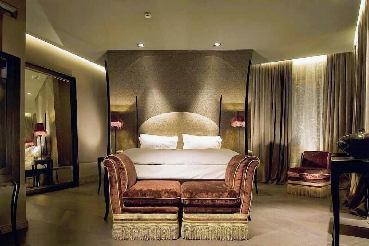 Ein Schlafzimmer mit einem großen Bett, zwei Nachttischen, einem Spiegel, einem Sessel und einem Schreibtisch.