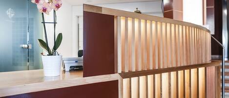 Una recepción con diseño de listones de madera, una orquídea en maceta y un interior moderno con un puerta de cristal y una escalera al fondo.