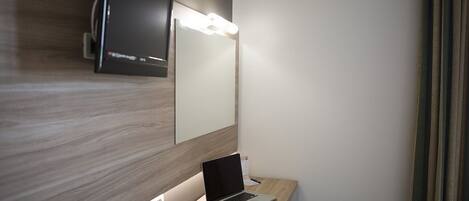 Una habitación de hotel moderna con un escritorio de madera, una computadora portátil y un televisor montado en la pared.