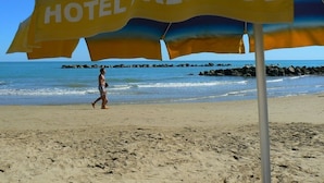 A beach with a large umbrella labeled "HOTEL RESTIGE" and a person walking. - Hotel Prestige (Montesilvano)