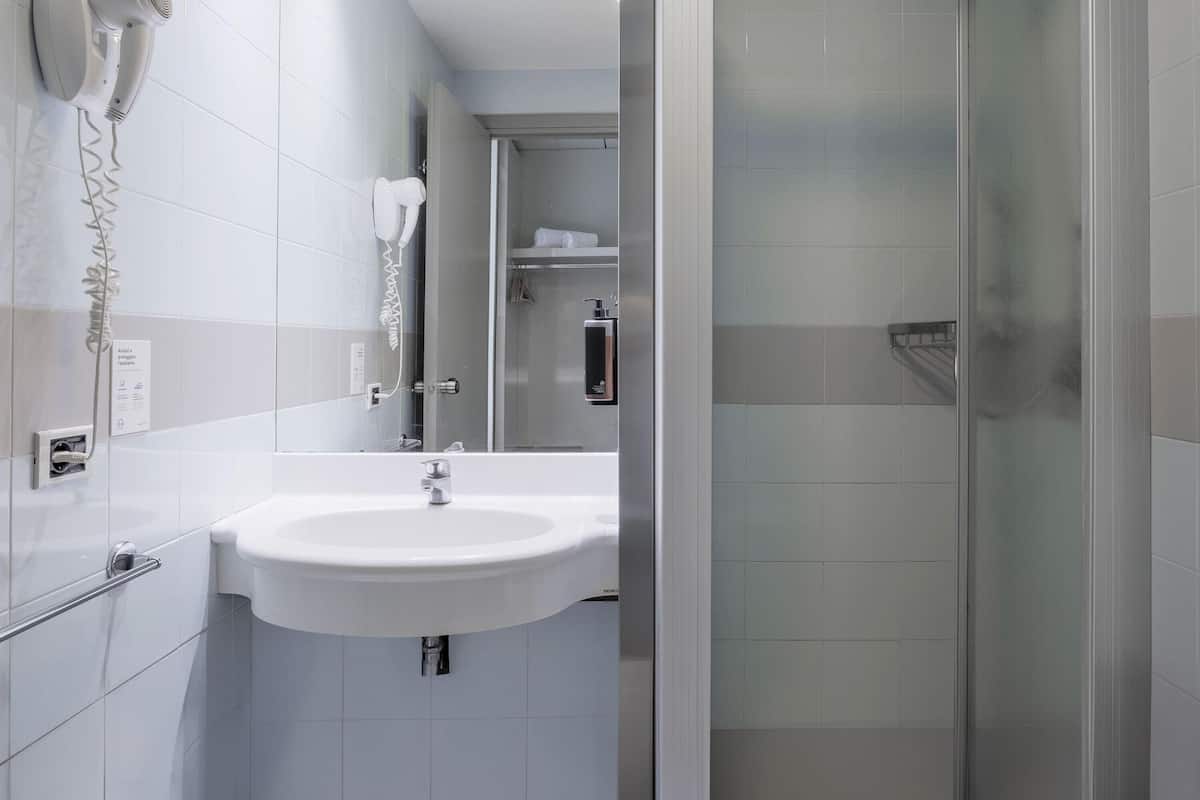 A modern bathroom with a white sink, a hairdryer, and a glass shower enclosure.