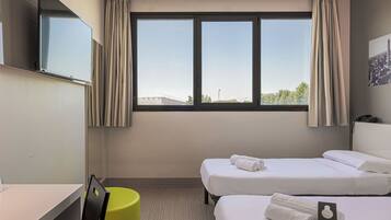 Ein Hotelzimmer mit zwei Betten, einem Schreibtisch, einem Stuhl, einem Fernseher und einem Fenster mit Vorhängen.