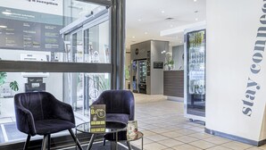 A reception area with two black chairs, a small table, and a glass wall displaying a menu. - B&B Hotel Bologna (Castel Maggiore)