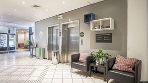 A modern lobby with a reception desk, two elevators, a vending machine, and a seating area with a potted plant. - B&B Hotel Bologna (Castel Maggiore)