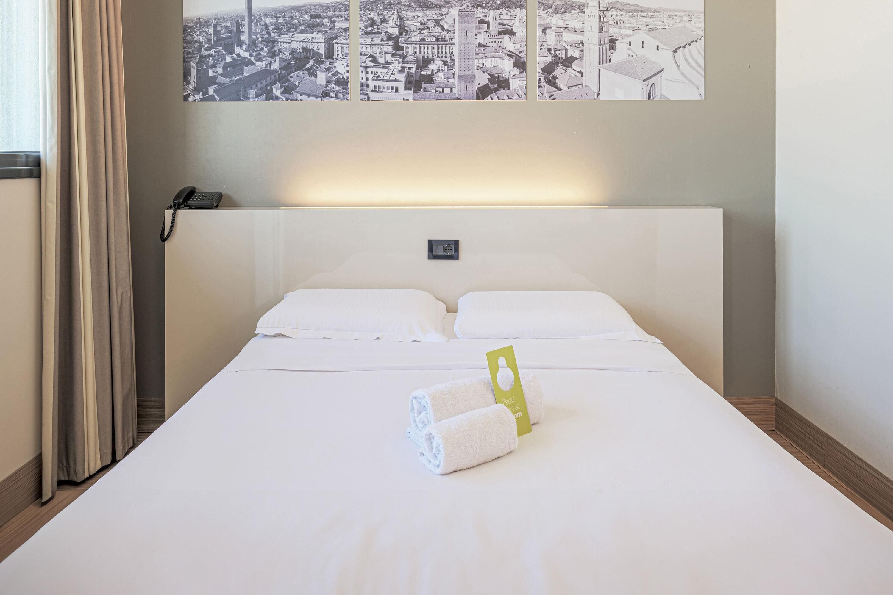 Ein Hotelzimmer mit einem großen Bett, weißer Bettwäsche, Blick auf die Stadt, einem Telefon auf dem Nachttisch und einem grünen Anhänger am Bett.