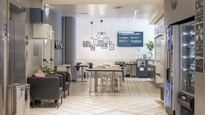 A hotel lobby with seating areas, a vending machine, and a digital information board. - B&B Hotel Bologna (Castel Maggiore)