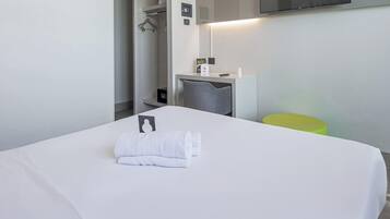 Una camera d'albergo con un letto ben rifatto, una piccola scrivania con una sedia, uno specchio e una televisione fissata alla parete.