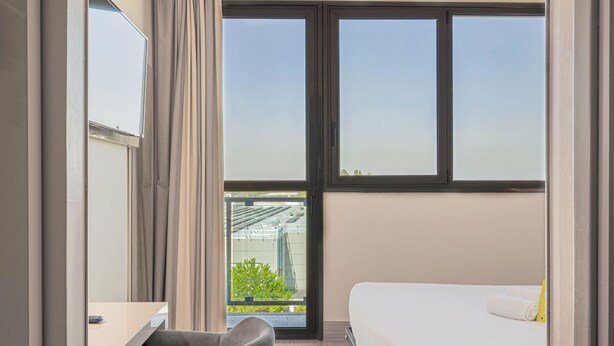 A modern hotel room with a large window, a desk, a chair, and a bed. - B&B Hotel Bologna (Castel Maggiore)