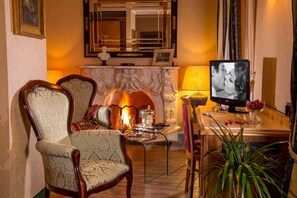 A cozy living room with a fireplace, two upholstered chairs, a glass coffee table, and a television. - Hotel Colonna (Frascati)