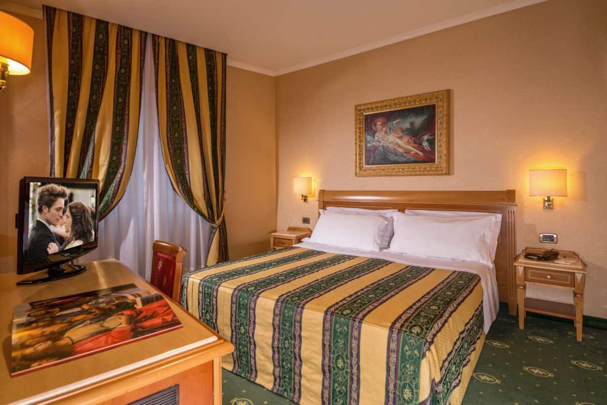A hotel room with a large bed, two bedside tables, a television, and a painting on the wall.