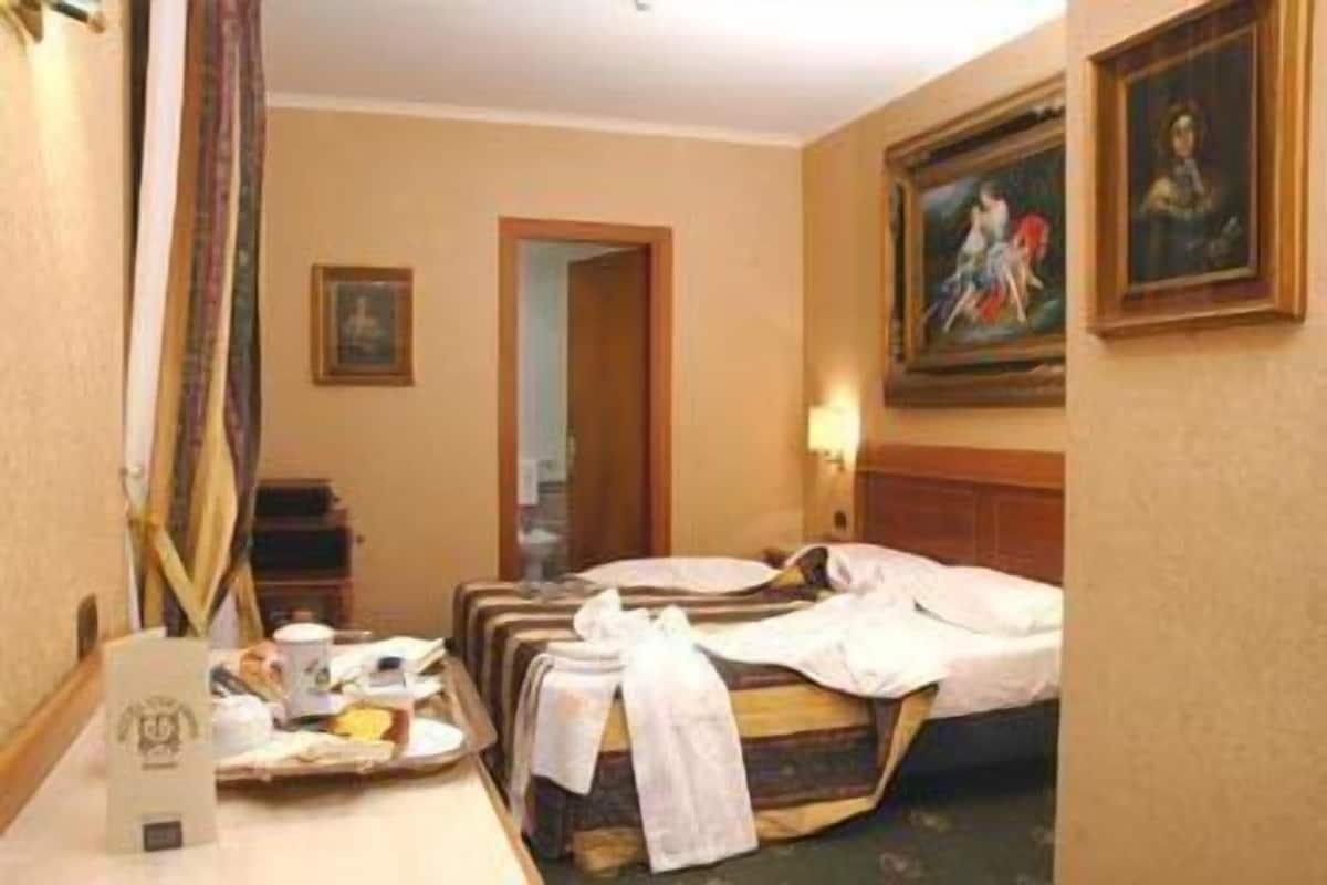 A hotel room with a bed, a desk with a tray of breakfast items, a painting on the wall, and a door leading to another room.