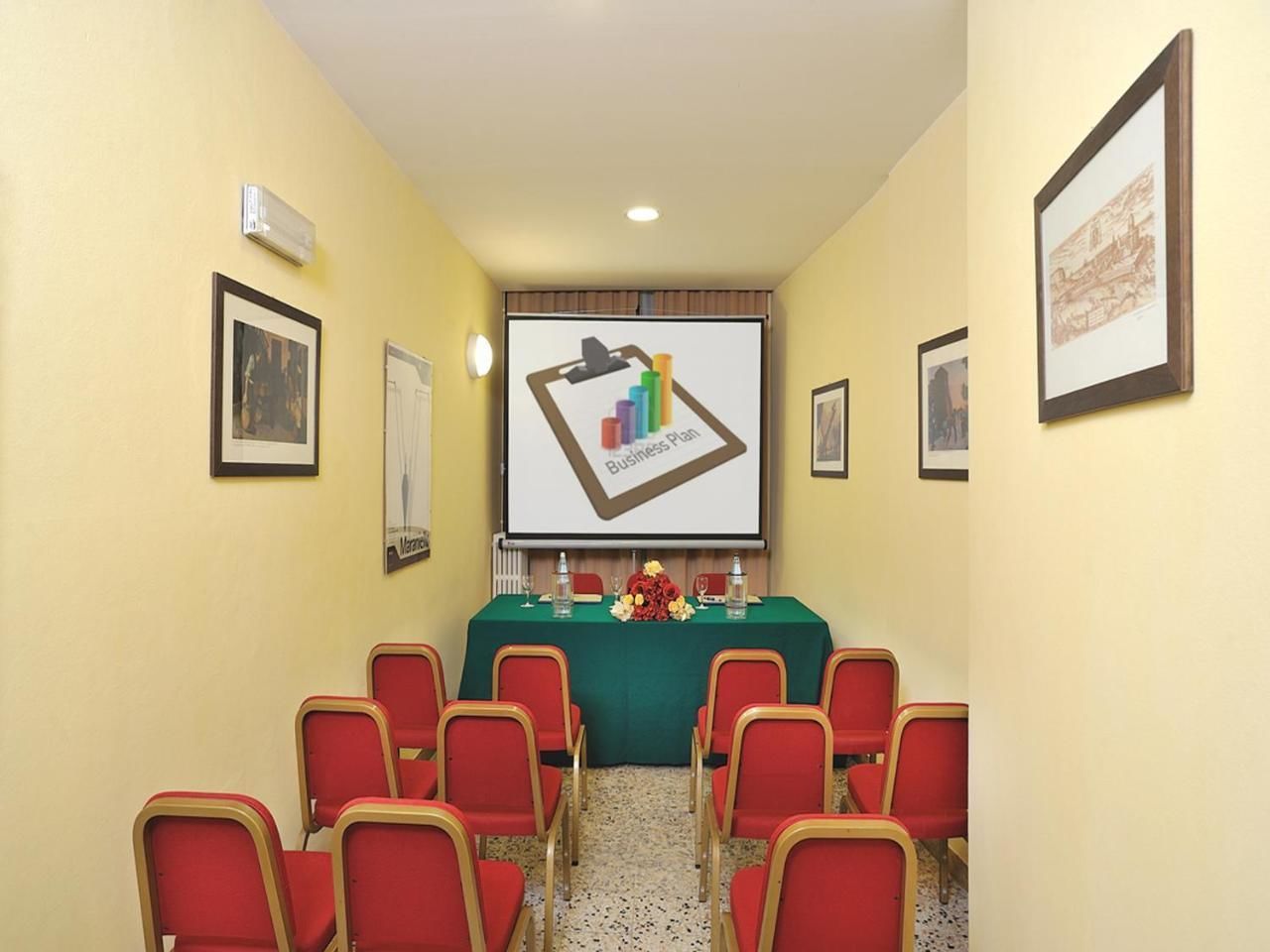 A conference room with a projector screen displaying a business plan, red chairs, and a table with floral arrangements.