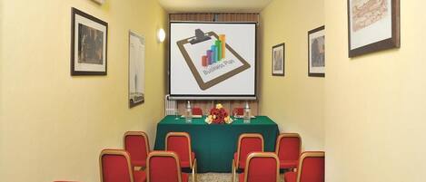 A conference room with a projector screen displaying a business plan, red chairs, and a table with floral arrangements.