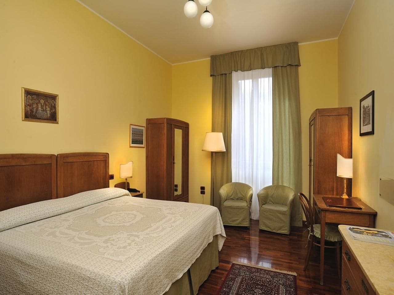 Ein Hotelzimmer mit einem großen Bett, zwei Stühlen, einem Schreibtisch und einem Fenster mit Vorhängen.