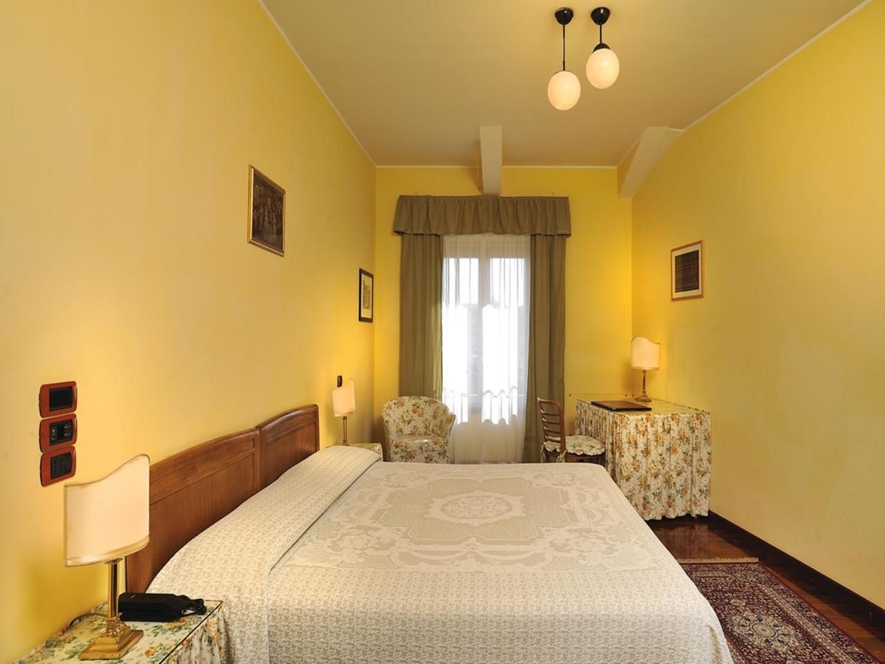 A hotel room with a large bed, two bedside tables with lamps, a chair, and a window with curtains.