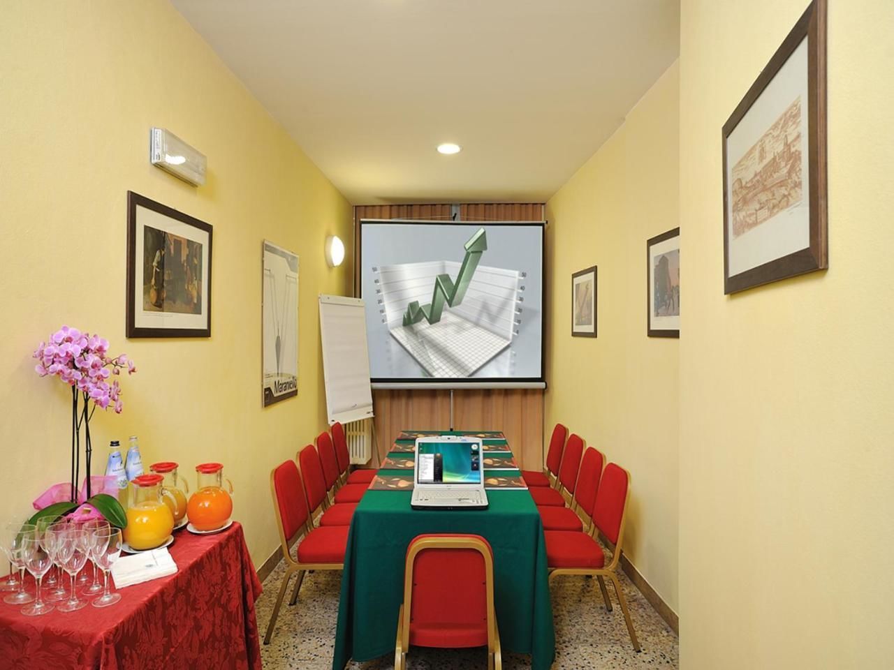 A conference room with a long table, red chairs, a laptop, and a projector screen displaying a graph.