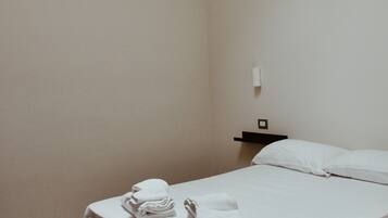 Une chambre d’hôtel simple et propre, avec un lit bien fait, une petite table de chevet et une lampe fixée au mur.
