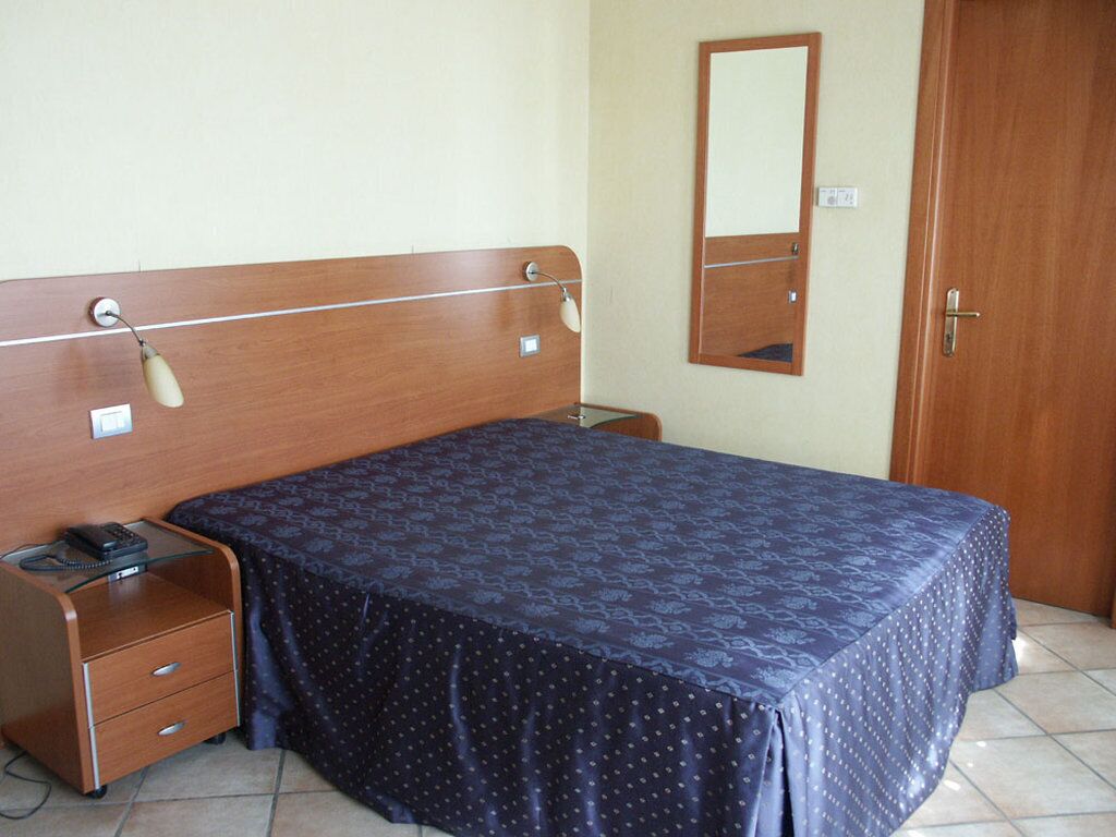 Un dormitorio con cabecera de madera, mesita de noche con lámpara, espejo y puerta.