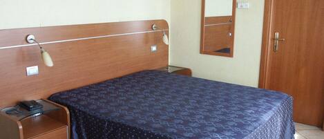 Un dormitorio con cabecera de madera, mesita de noche con lámpara, espejo y puerta.