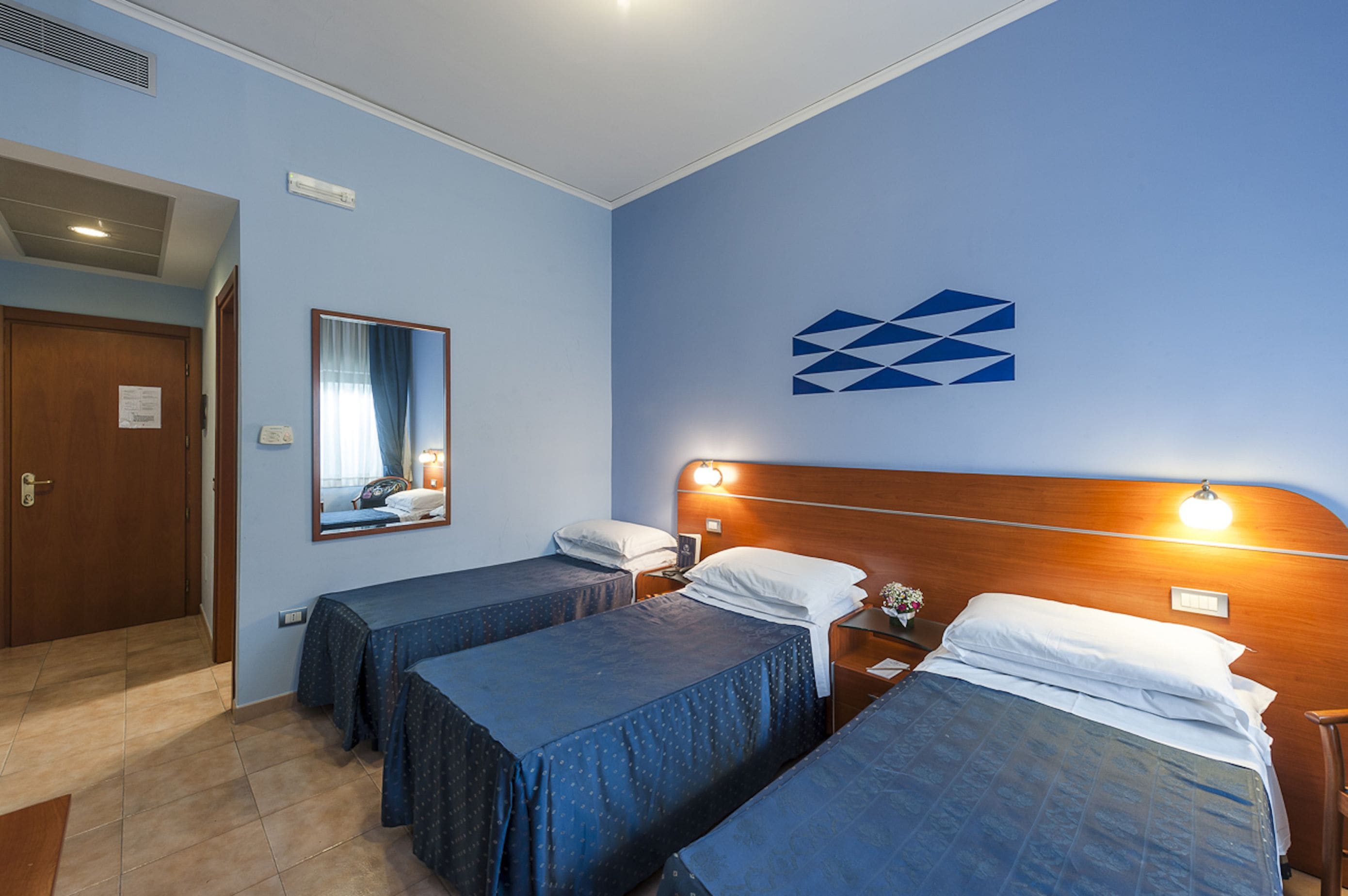 Habitación de hotel con dos camas individuales, un cabecero de madera, un espejo y un logotipo en la pared.