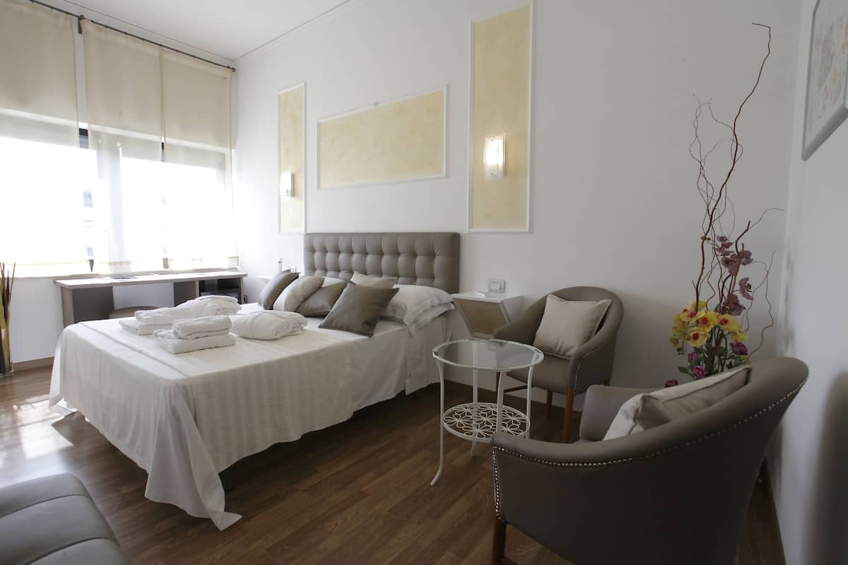 A hotel room with a bed, two chairs, a small round table, and a decorative plant.