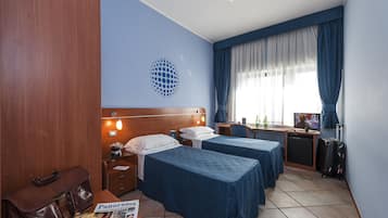 Habitación de hotel con dos camas, un escritorio, televisión, refrigerador pequeño y maleta.
