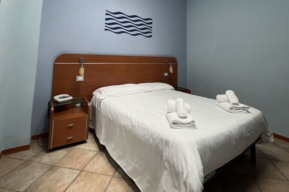 A hotel room with a wooden headboard, a bed with white linens, a bedside table with a phone, and a wall-mounted light fixture.