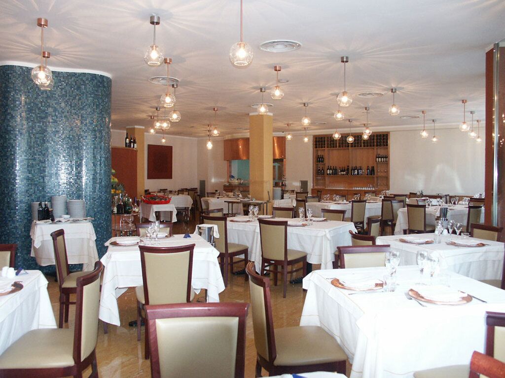 Un restaurante con varias mesas y sillas, una amplia pared de mosaico azul y lámparas colgantes.