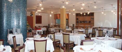 Un restaurante con varias mesas y sillas, una amplia pared de mosaico azul y lámparas colgantes.