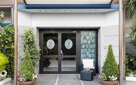 A hotel entrance with a covered entrance, glass doors, and potted plants.