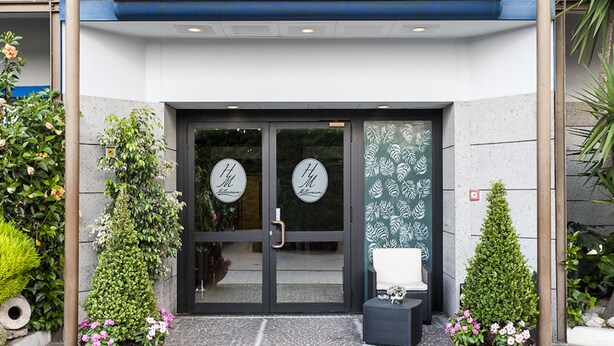 Ingresso di un hotel con portico, vetrate e piante in vaso.