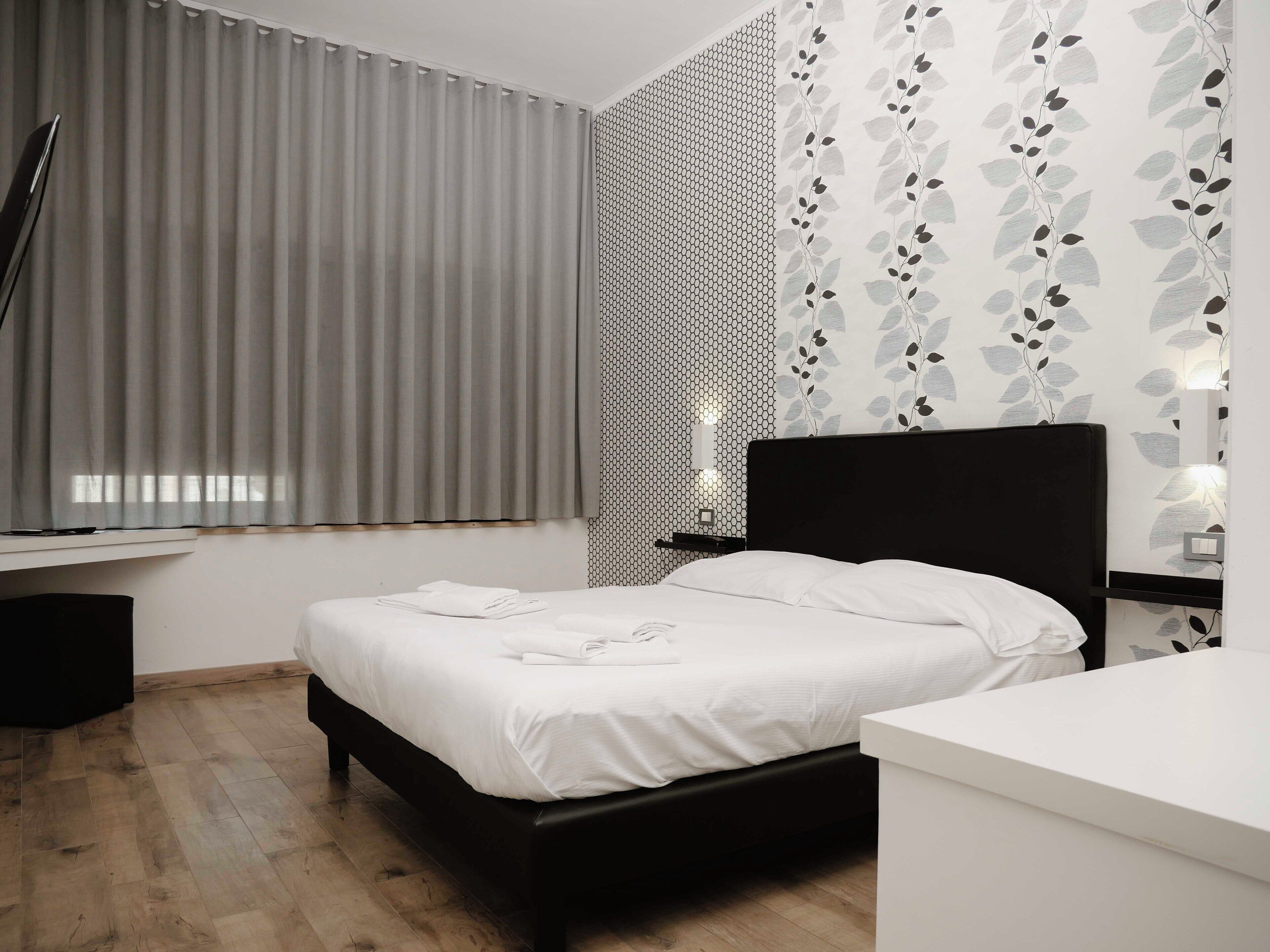 Un dormitorio moderno con cama, mesita de noche y ventana con cortinas.