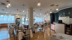 Un ristorante spazioso con diversi tavoli e sedie, un bancone con una cassa e luci a sospensione.
