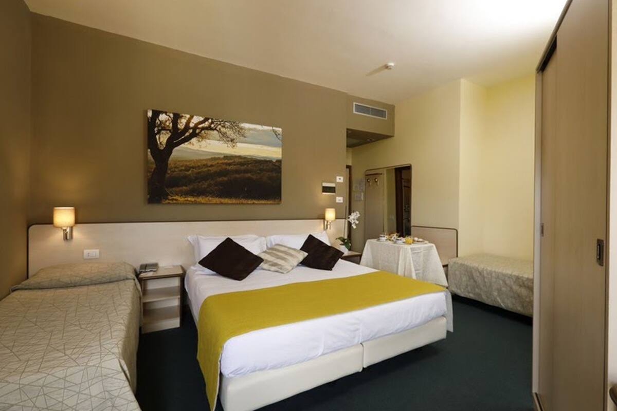 Une chambre d’hôtel avec un grand lit, un lit plus petit, un bureau avec une lampe et un tableau au mur.